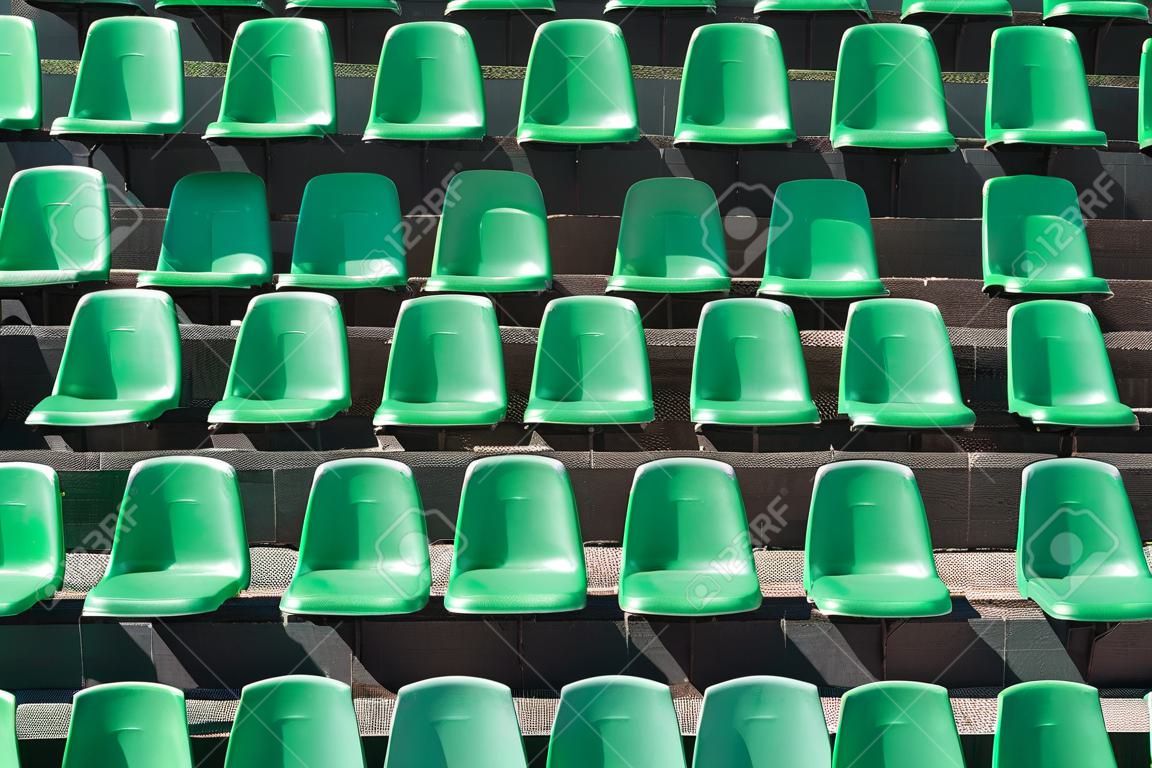 Image of green plastic stadium seats in rows. The seats are filled the frame as background. This is a day shot of an empty stadium.