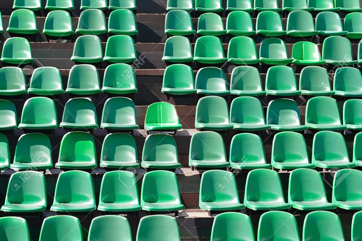 Imagen de asientos del estadio de plástico verde en filas. Los asientos están llenos del marco como fondo. Esto es un tiro día de un estadio vacío.