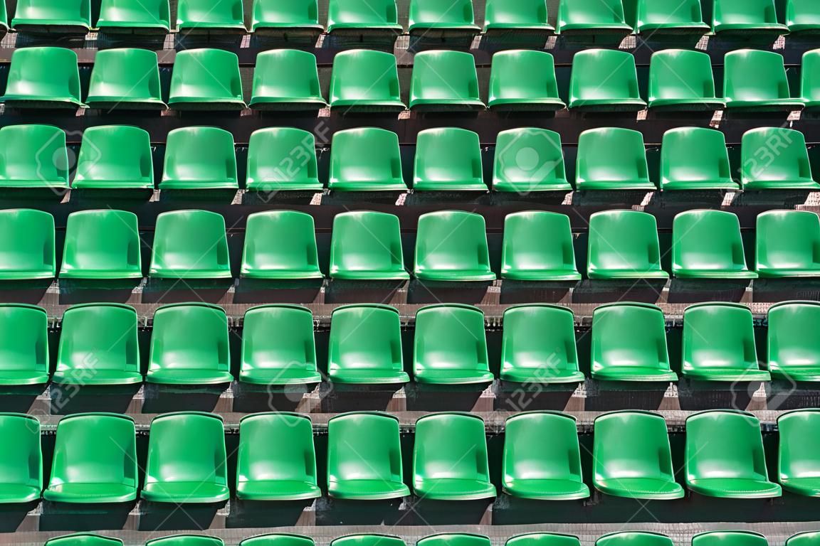 Imagen de asientos del estadio de plástico verde en filas. Los asientos están llenos del marco como fondo. Esto es un tiro día de un estadio vacío.