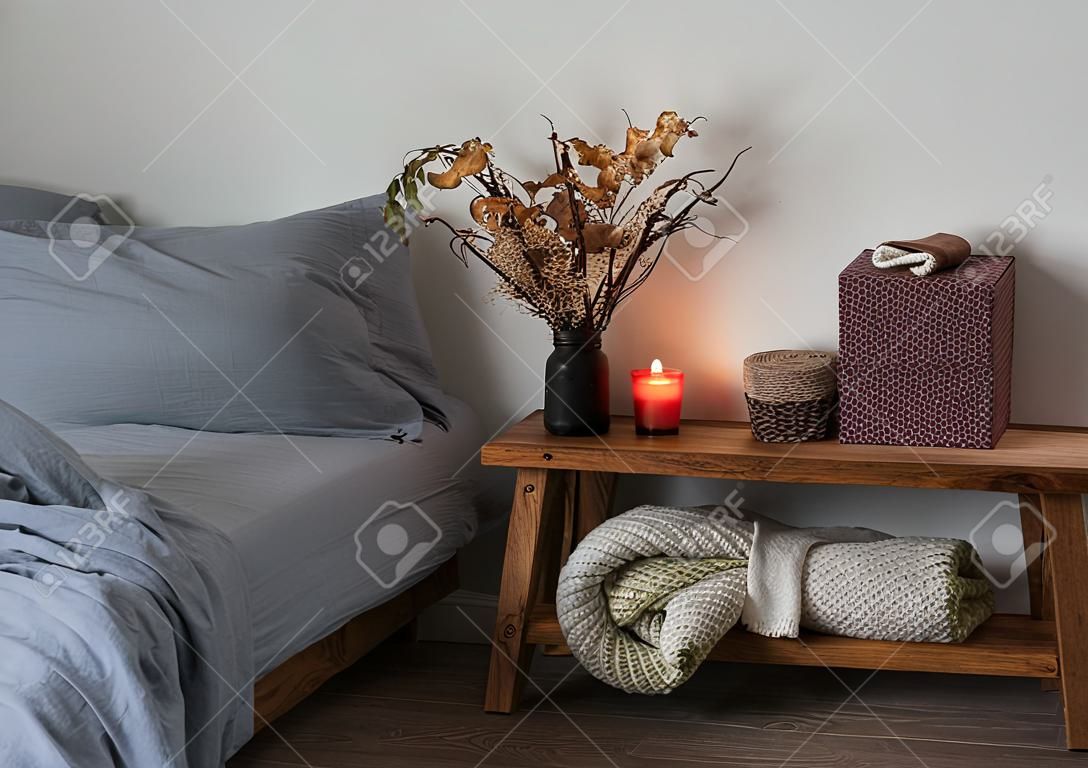 Cozy home evening - a bed with linen, a plaid, a wooden bench with autumn decor and lit candles