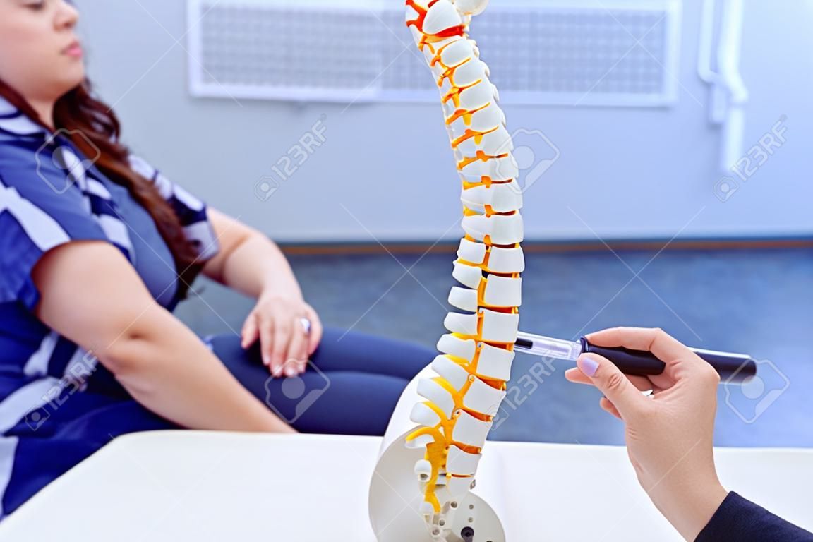 Closeup medical doctor woman pointing on spine model and explaining female patient her problem. Healthcare concept