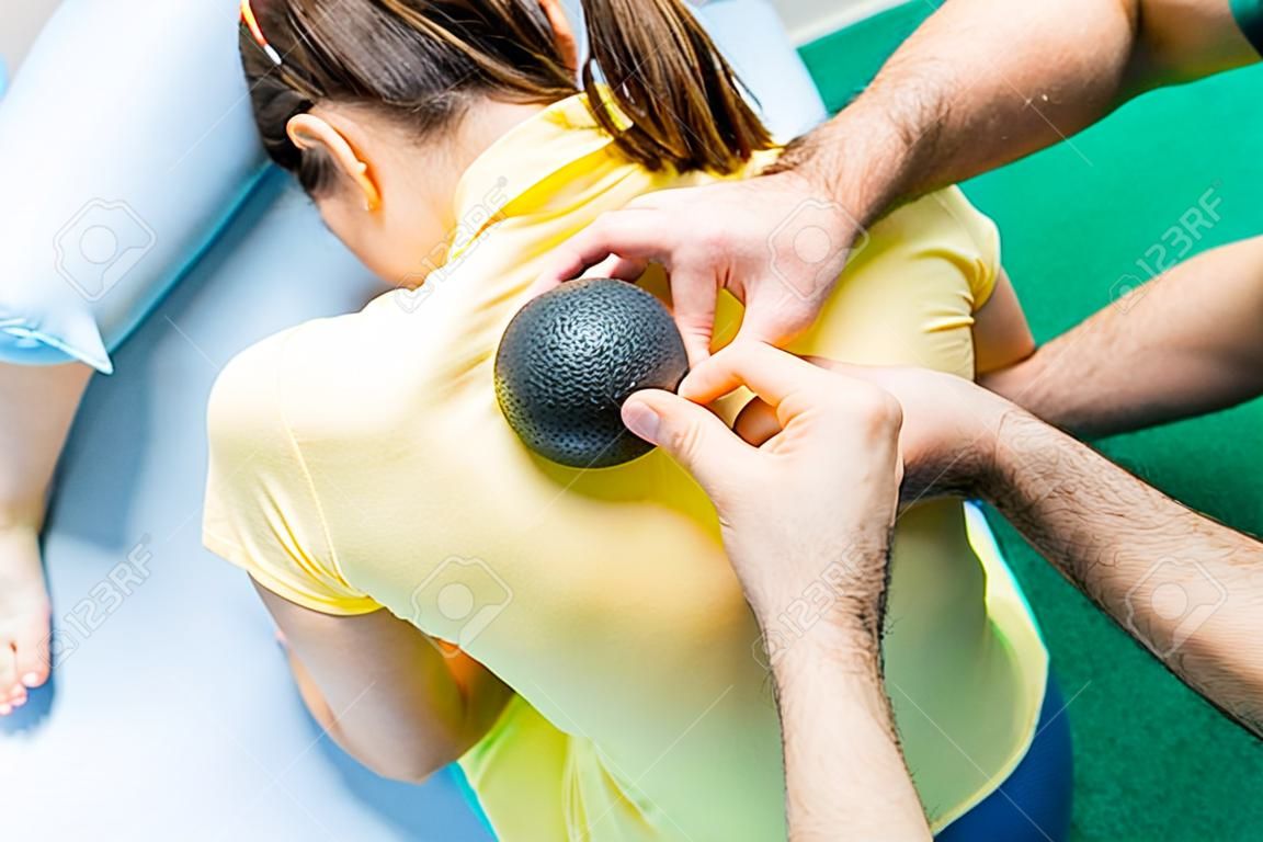 Woman at the physiotherapy receiving ball massage from therapist. A chiropractor treats patient's thoracic spine in medical office. Neurology, Osteopathy, chiropractic. Selective focus, Close up