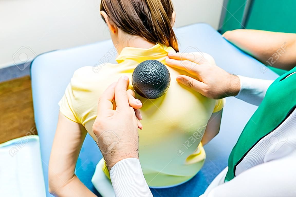 Woman at the physiotherapy receiving ball massage from therapist. A chiropractor treats patient's thoracic spine in medical office. Neurology, Osteopathy, chiropractic. Selective focus, Close up