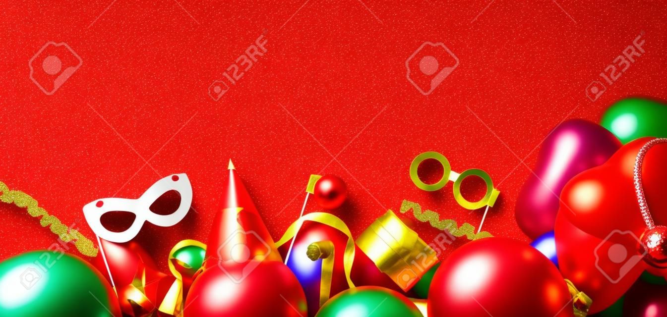 Bright red Festive background with party tools and decoration - baloons, funny carnival masks, festive tinsel. Happy birthday greeting card. Design concept. Wide. Select focus, place for text