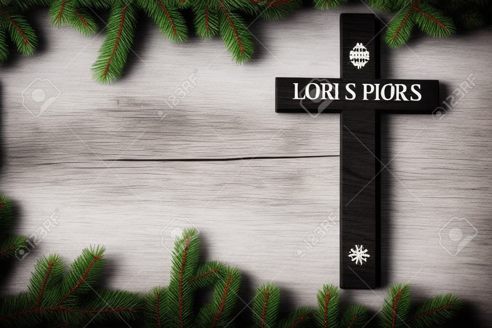 Zwart houten kruis met de Heren gebed op witte houten plank met dennenboom takken achtergrond