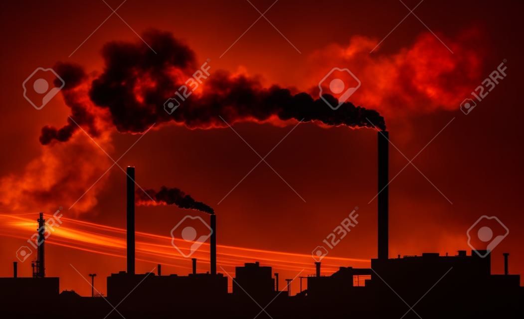 Silhouette of a factory with smoke coming out of chimneys.