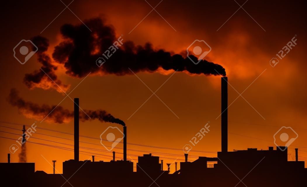 Silhouette of a factory with smoke coming out of chimneys.
