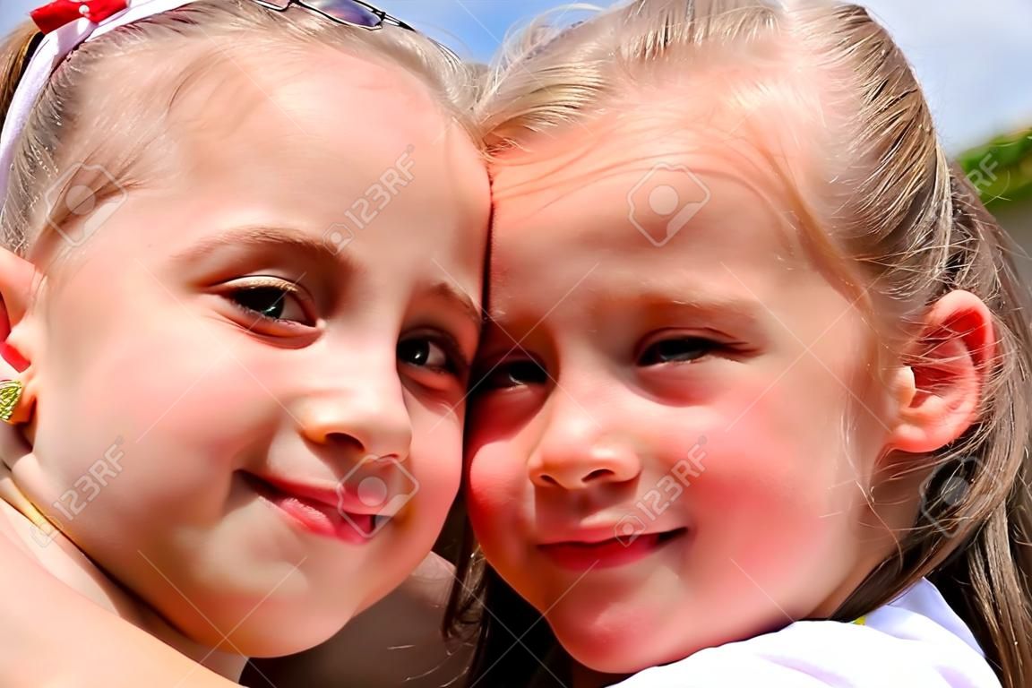 Two sisters hug one another outdoors, happy family. Close up faces.