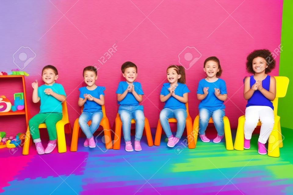 Kinder sitzen auf den bunten Stühlen und klatschen in die Hände