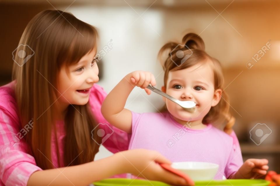 子供の屋内キッチンでスプーンで食べる女の子