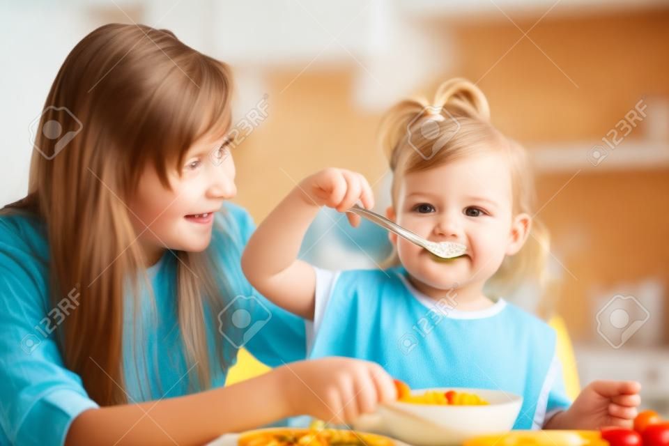 chica chico come con la cuchara en el interior en la cocina