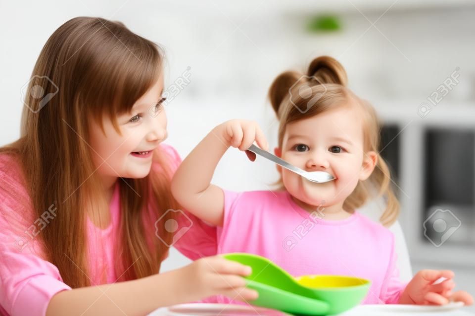 ребенок девочка ест с ложкой в ​​помещении при кухне
