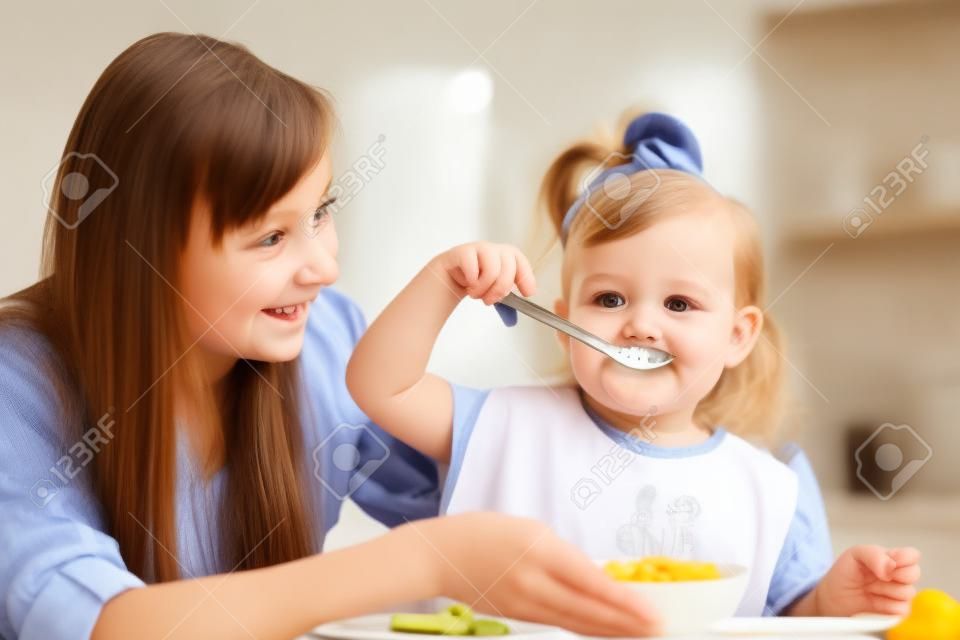 chica chico come con la cuchara en el interior en la cocina