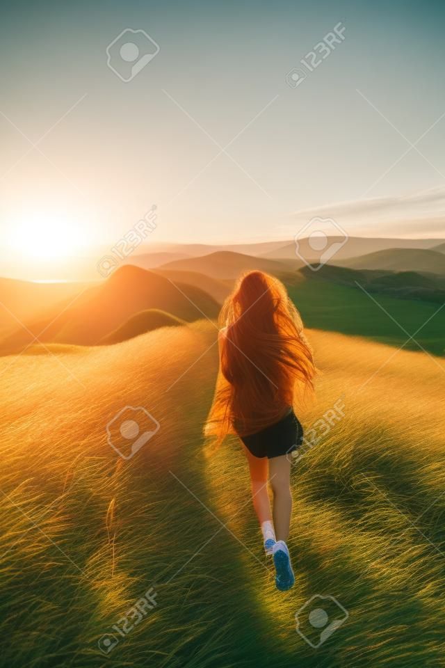 Glückliche junge Frau läuft auf Feder Gras Feld in Sonnenuntergang Licht. Naturlebensstil und herrlicher Ausblick. Langes schwarzes Haar mit farbigen Schlössern