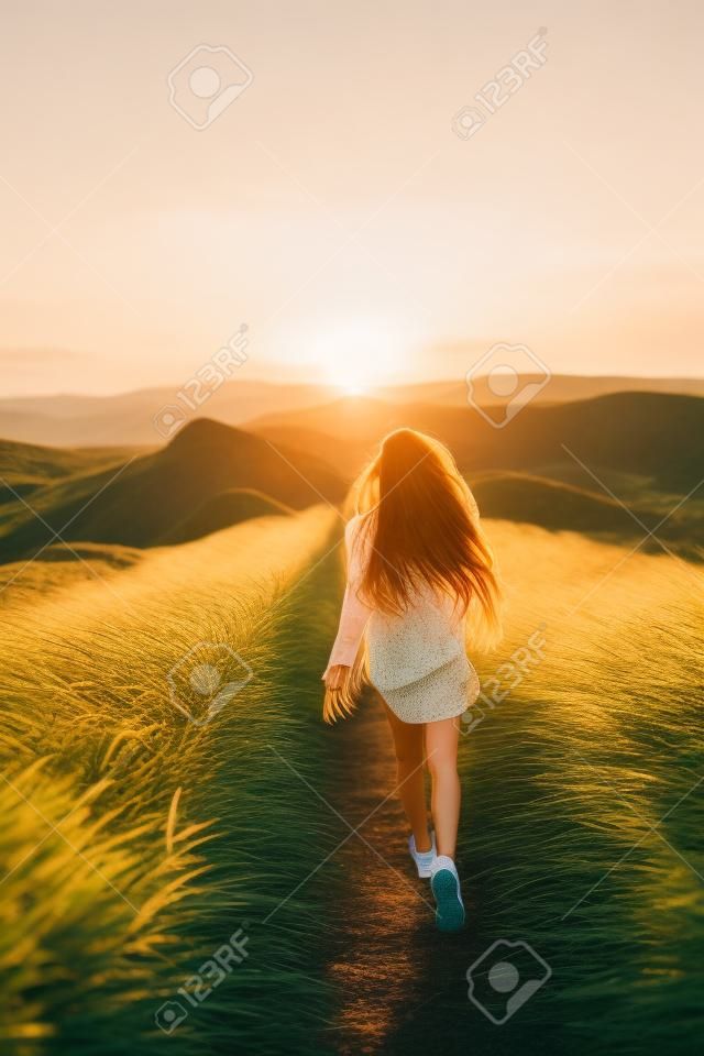 Glückliche junge Frau läuft auf Feder Gras Feld in Sonnenuntergang Licht. Naturlebensstil und herrlicher Ausblick. Langes schwarzes Haar mit farbigen Schlössern