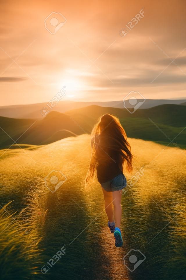 Happy young woman running on feather grass field in sunset light. Nature lifestyle and amazing view around. Long black hair with colored locks