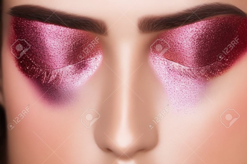 Feestelijke gloeiende oogschaduw make-up in bruine en roze kleuren met glanzende en glitter schittert close-up. Schoonheid trendy concept.