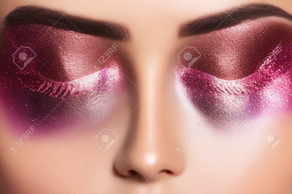 Festive glowing eyeshadow make up in brown and pink colors with shiny and glitter sparkles close up. Beauty trendy concept.