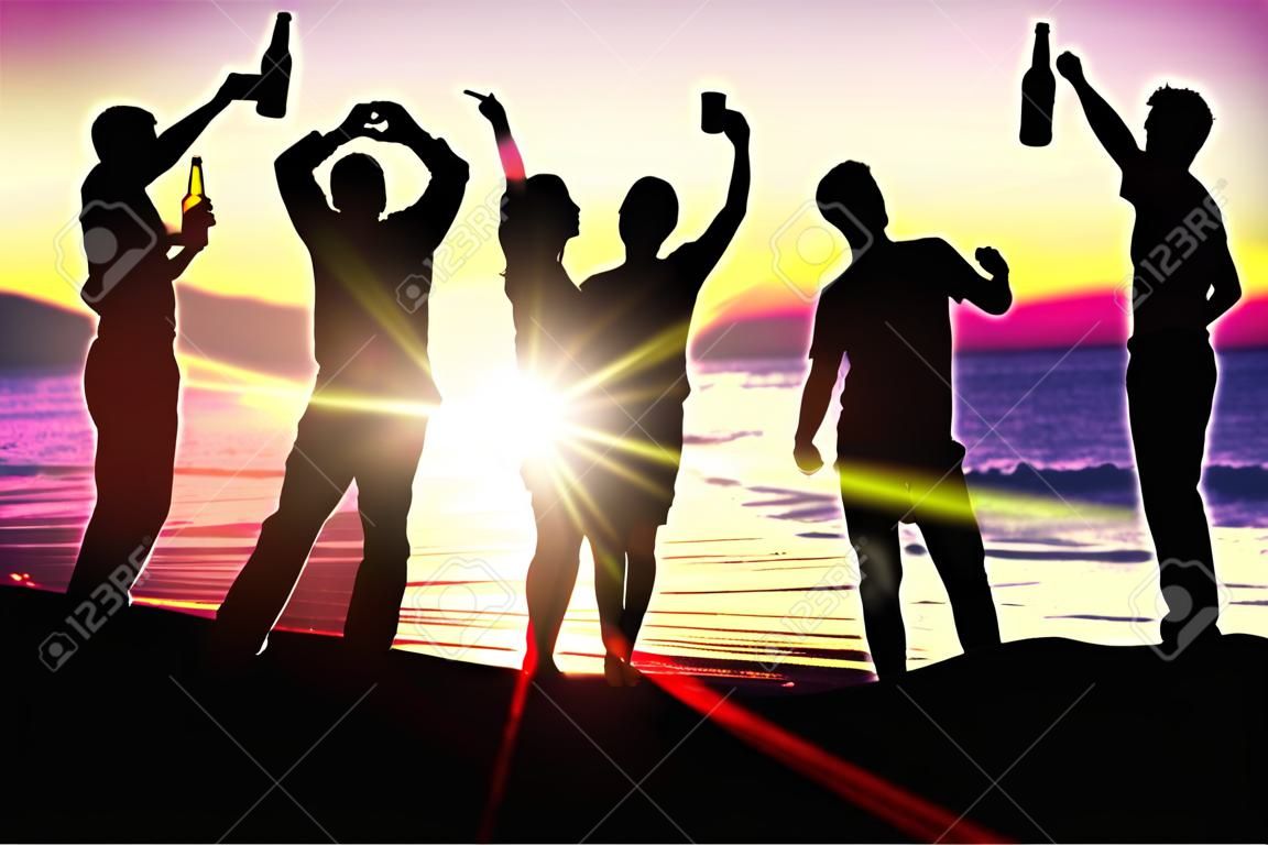 Mensen (twee koppels) op het strand hebben een feestje, drinken en hebben veel plezier in de zonsondergang (alleen silhouet van mensen te zien, mensen hebben flessen in handen met de zon schijnt door)
