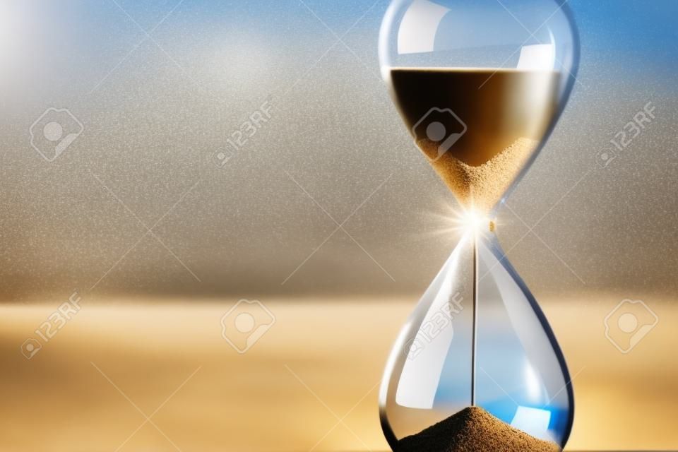 Moderne Sanduhr mit verschwommenem Fensterhintergrund - Sand rieselt durch die Glühbirnen eines Kristallsandglases. Jede Sekunde zählt. Symbol der Zeit. Countdown.