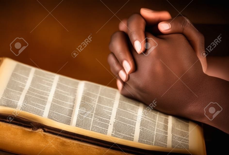 Manos rezando en una biblia abierta