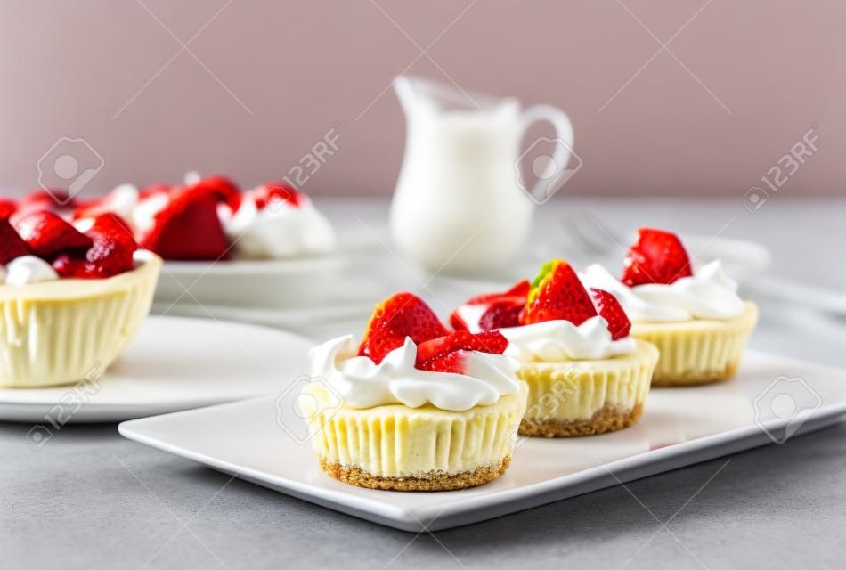 Minikäsekuchen mit Erdbeere und Schlagsahne auf einer Platte