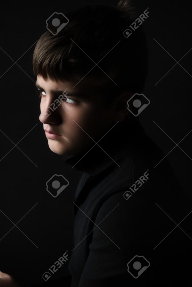 Sad Teenager ist auf dem schwarzen Hintergrund fotografiert. Er ist verärgert. Sie ist in schwarz tragen.