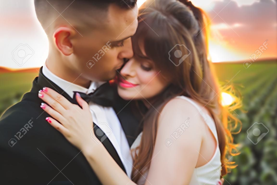 el novio está sosteniendo y besando a su novia en el fondo del atardecer.