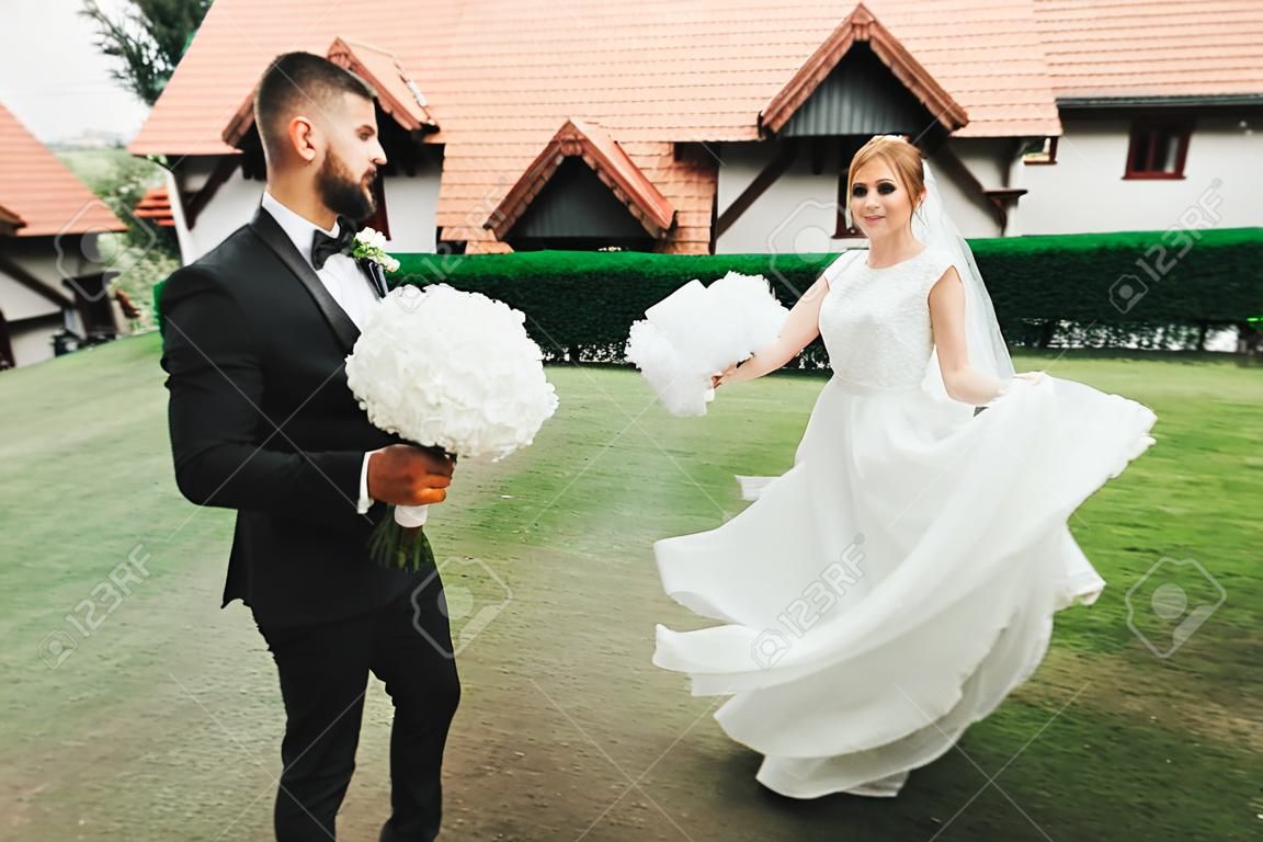 Stilvolles Paar glückliche Jungvermählten. Braut und Bräutigam im Park an ihrem Hochzeitstag mit Blumenstrauß