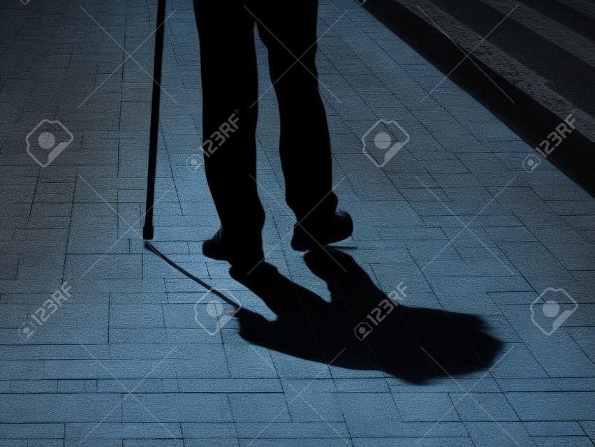 Silhueta do homem mancando que anda com a sombra longa da bengala no pavimento. Conceito para a deficiência, idade avançada, pessoa cega, vida dramática