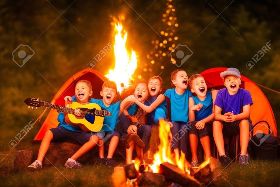 glückliche Kinder singen Lieder rund um Lagerfeuer