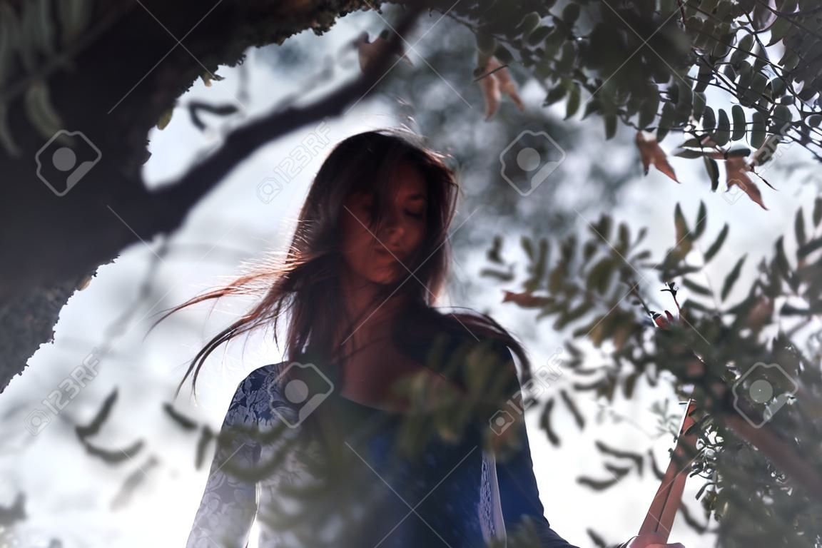 Beautiful brunette girl, portrait through the trees on a background of nature. Spring, beauty, fashion concept
