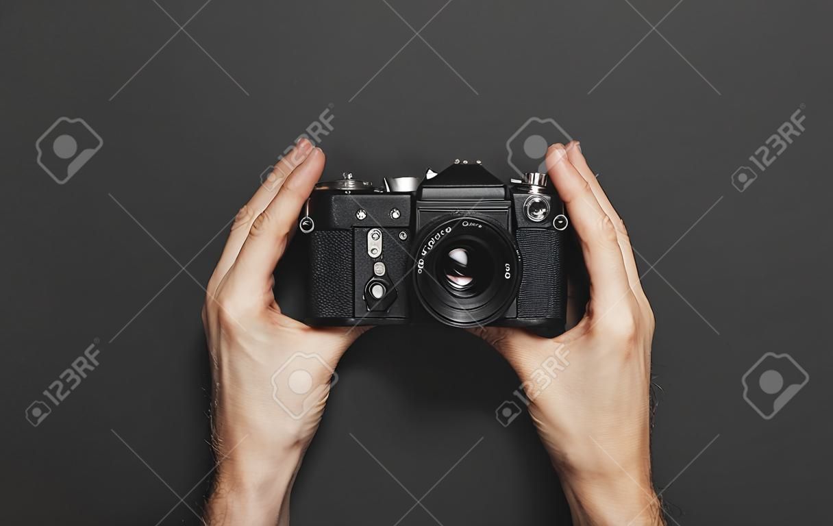 Le mani maschili tengono la vecchia fotocamera vintage su sfondo nero vista dall'alto piatto con spazio per la copia. Concetto per il fotografo, vecchia attrezzatura fotografica in stile minimalista