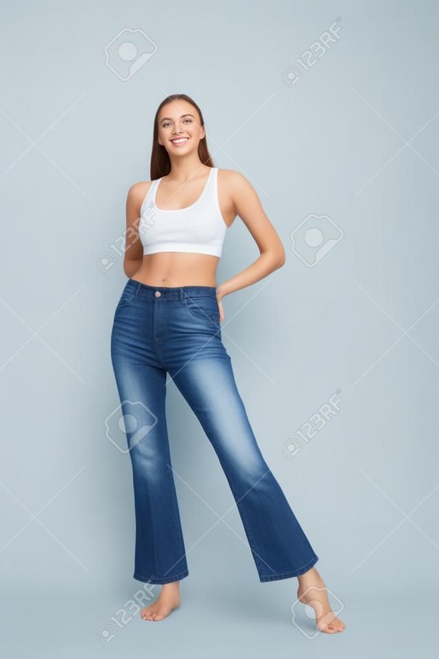 Girl in jeans and barefoot posing on a white background