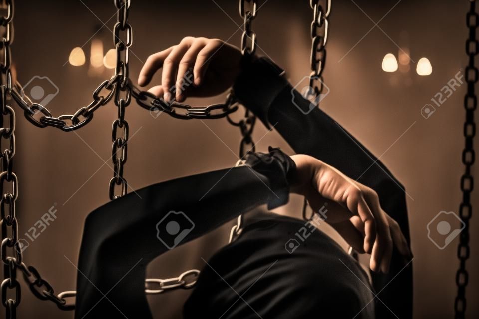 Manos de mujer esposada entre cadenas en la oscuridad