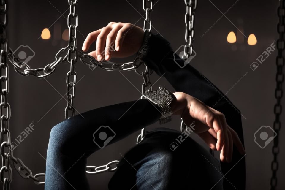 Hands of woman in handcuffs between chains in dark