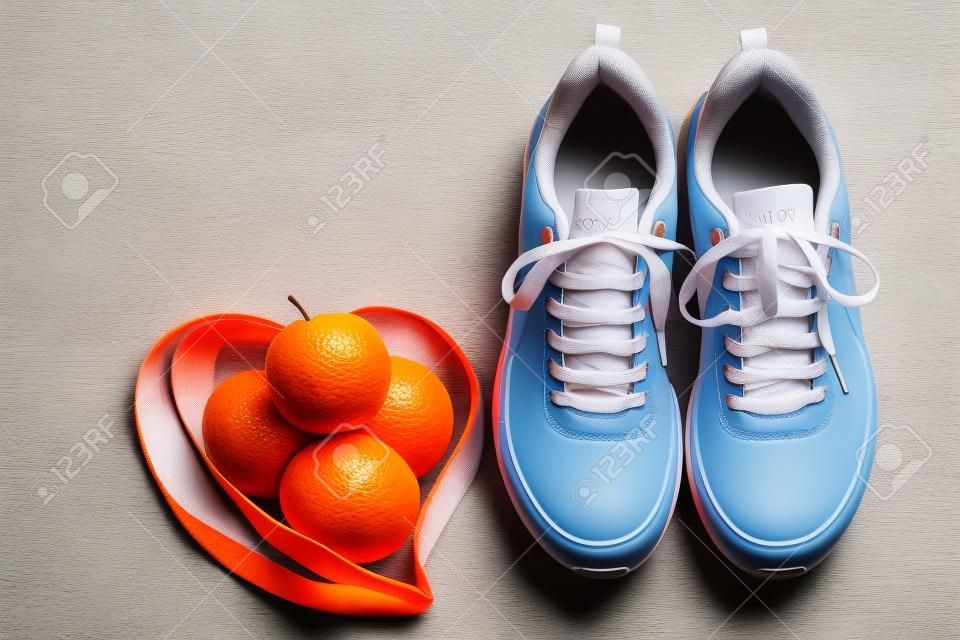 Orange sneakers, measuring tape and fruits apples and oranges on a blue background. Fitness sport equipment with copy space