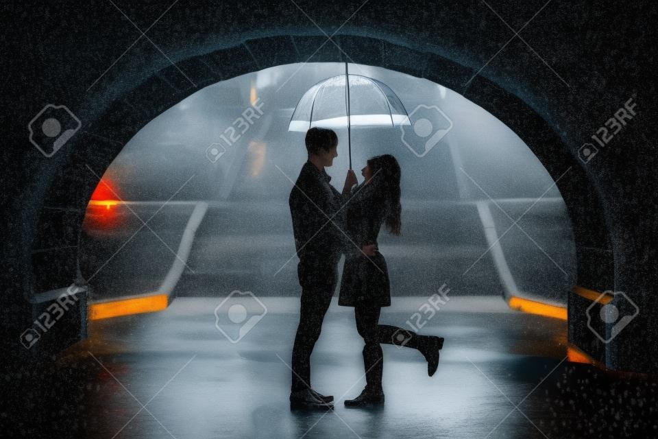 Couple d'amoureux étreignant sous un pont sur un jour de pluie - Silhouettes de l'homme et la femme sur une date romantique sous la pluie, en riant et amusent