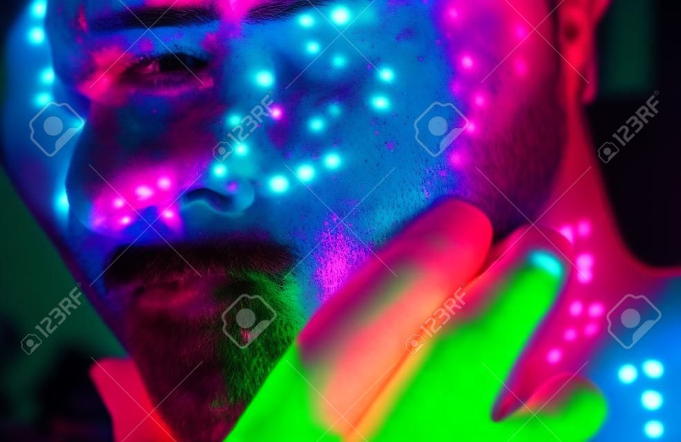 Knappe jongen danst op het feestje met fluorescerende schilderijen op zijn gezicht