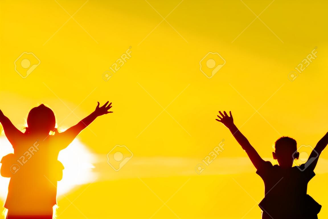 A silhueta da família da mãe e da criança em pé vê o pôr do sol e o céu em laranja à noite.