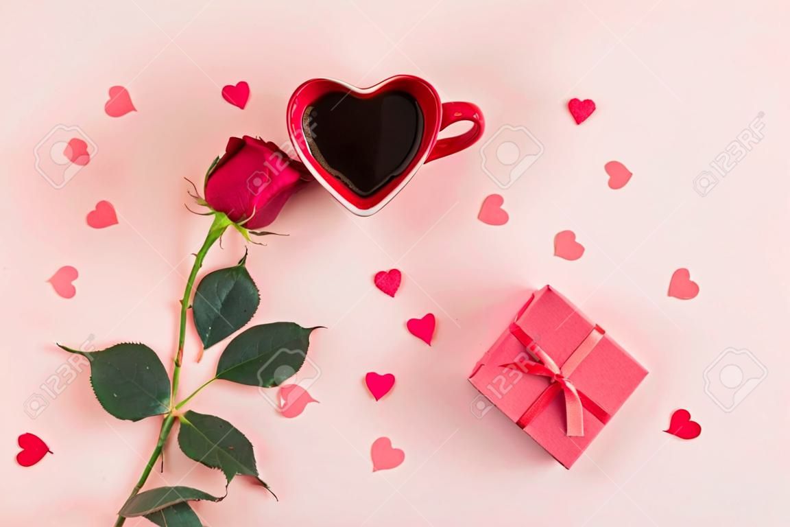 Valentijnsdag achtergrond. Hartvormige beker van zwarte koffie, kleine hartjes, roos en geschenk doos op pastel roze achtergrond. Valentijnsdag, jubileum, verjaardag concept. Platte lay, top view