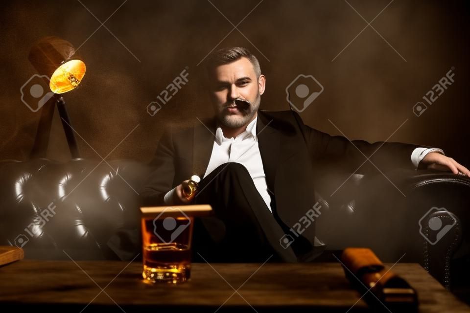 Hombre atractivo con cigarro y un vaso de whisky
