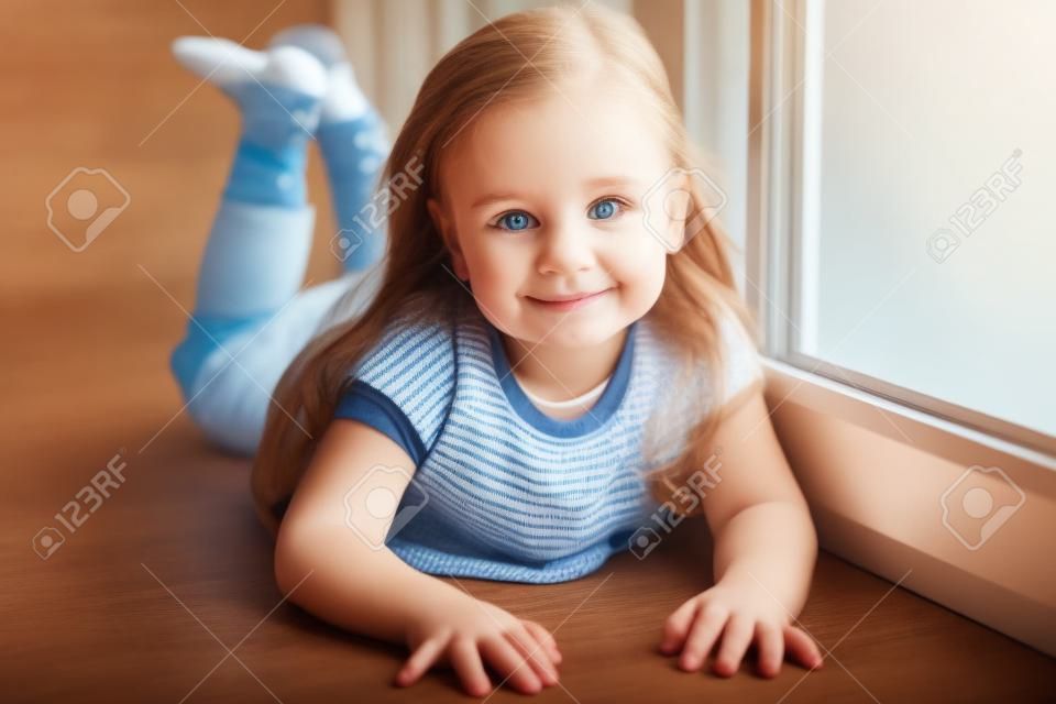 Little smiling child girl watching out the window