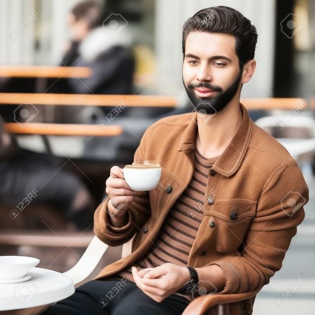 Young fashion man with beard drinking espresso coffee in the city cafe during lunch time