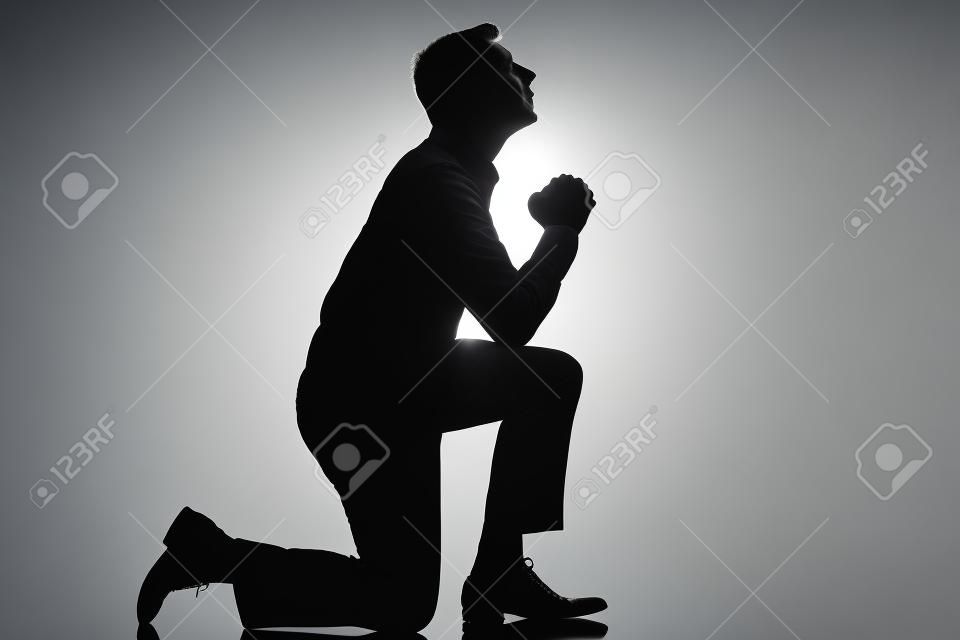 un hombre caucásico de rodillas orando silueta de cuerpo entero en el estudio de fondo blanco aislado