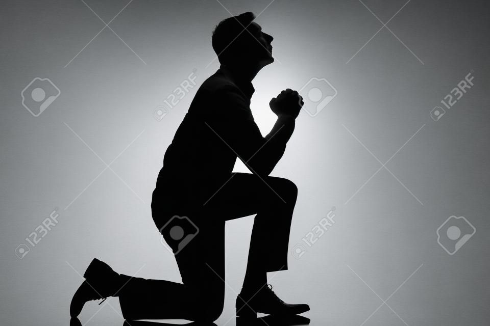 un hombre caucásico de rodillas orando silueta de cuerpo entero en el estudio de fondo blanco aislado
