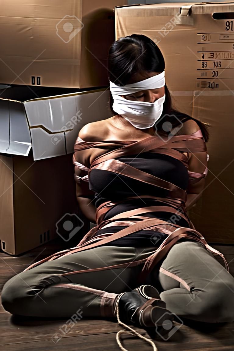 A young woman tied-up, blind folded and muted in old room. Low key setting