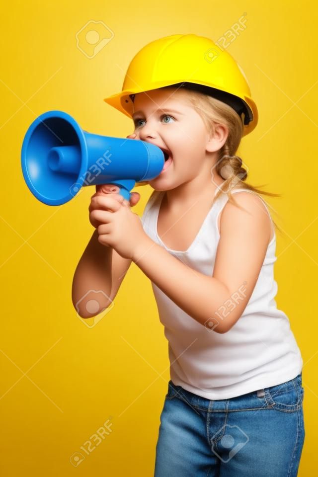 Jolie constructeur petite fille dans un casque jaune criant dans le haut-parleur, sur fond blanc