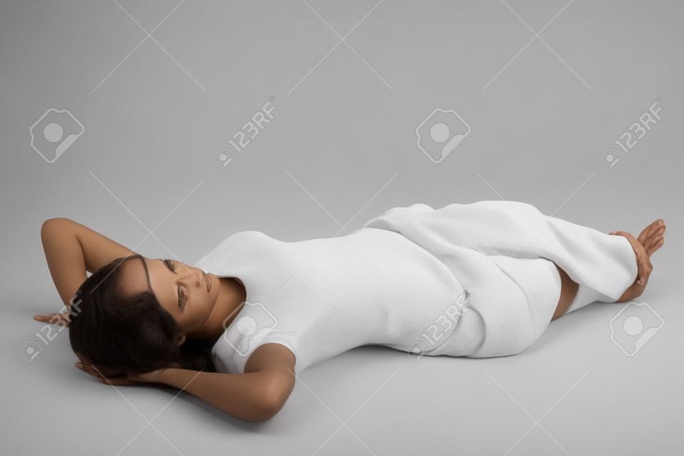 全长的女人躺在地板上，双手背在头上，在白色背景下休息