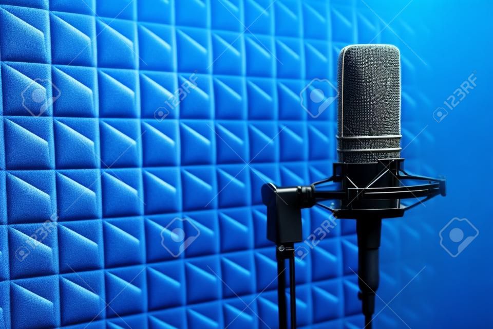 Studio condenser microphone on blue acoustic foam panel background with copy space on left